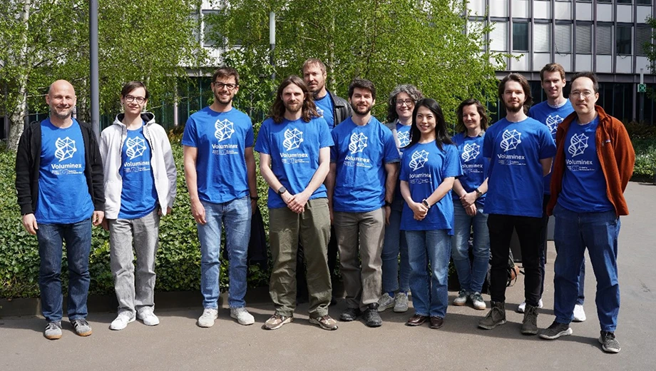 A group of people wearing matching T-shirts taking a group photo out side. 